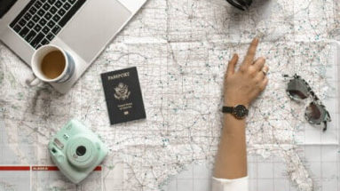 A person looking at a map determines where to go on their journey. They also have a passport, laptop computer, and camera. When embarking on a journey, you need a strategy, such as creating a successful content marketing strategy.