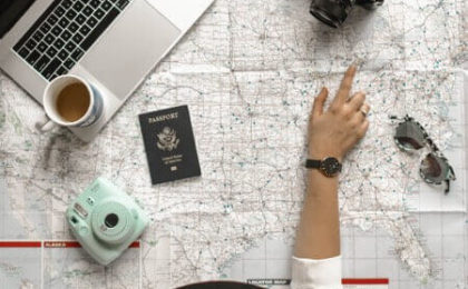 A person looking at a map determines where to go on their journey. They also have a passport, laptop computer, and camera. When embarking on a journey, you need a strategy, such as creating a successful content marketing strategy.